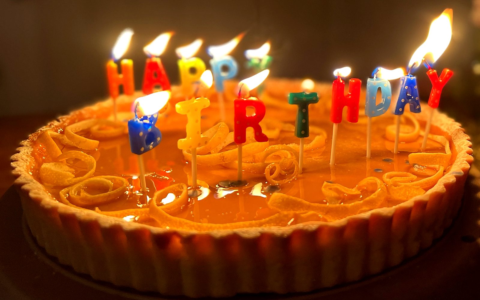 Lemon tart with curled citrus peel and lit birthday candles