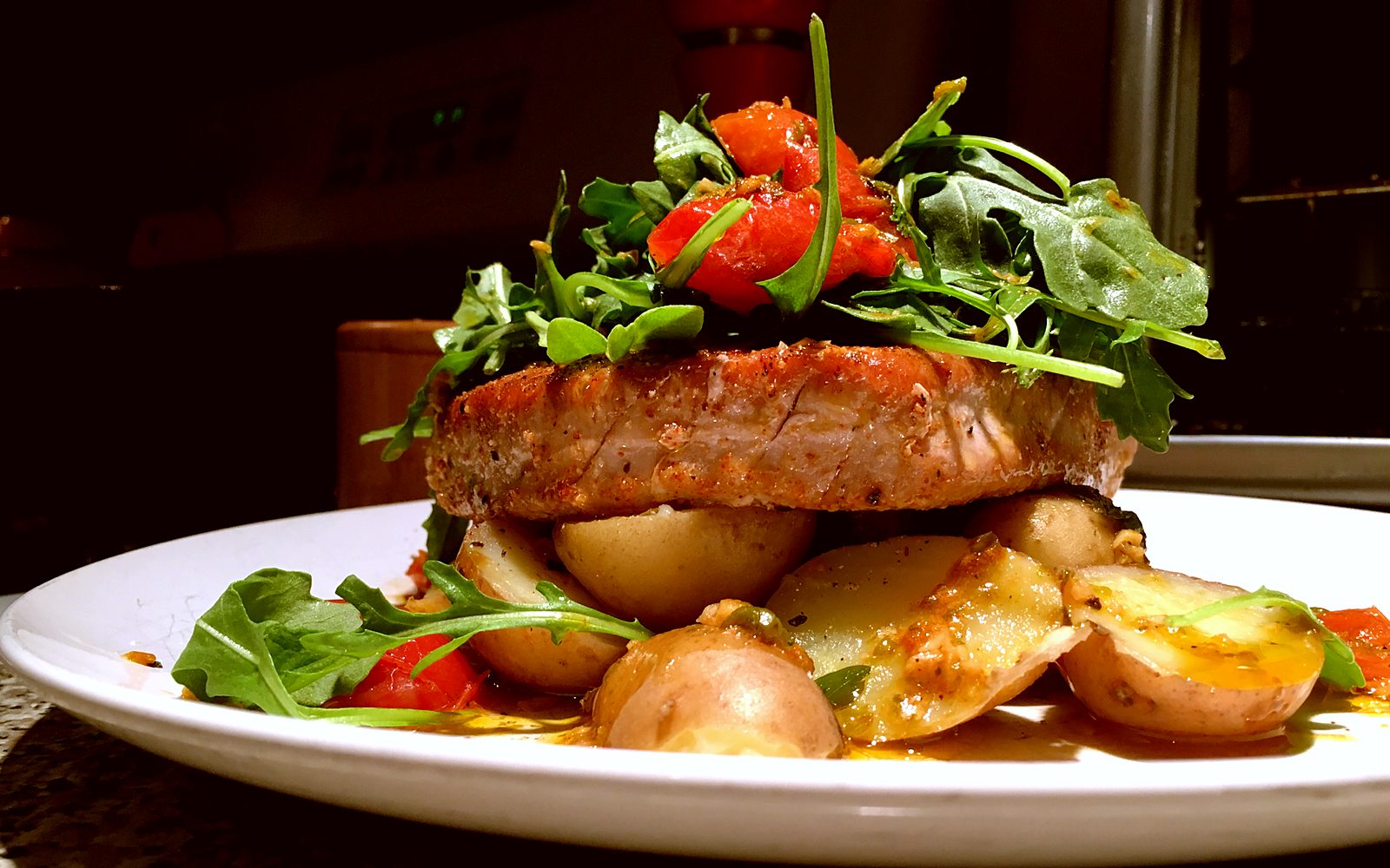 Seared tuna steak over potatoes with arugula and roasted tomatoes